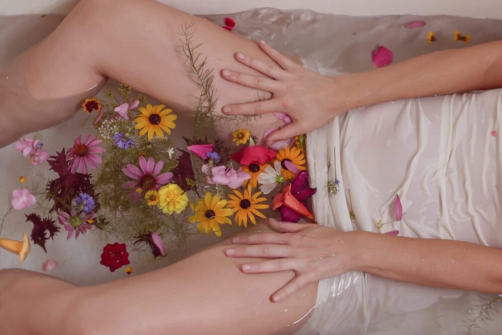 person in bathtub with vibrant wildflowers in the water between legs